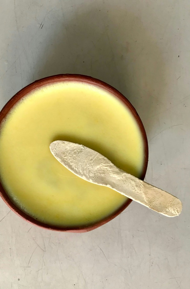 Mishti doi set in a clay pot, a wooden spoon lifting the surface